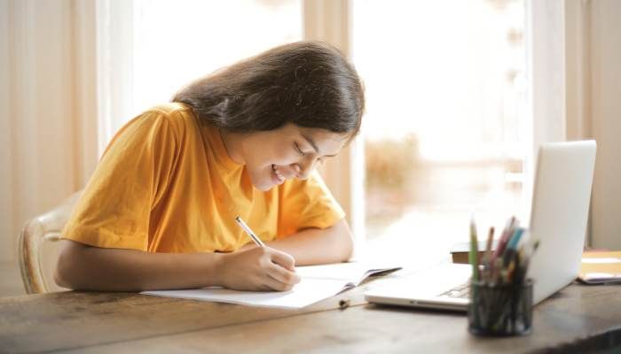 Young girl writing in booklet sitting at desk